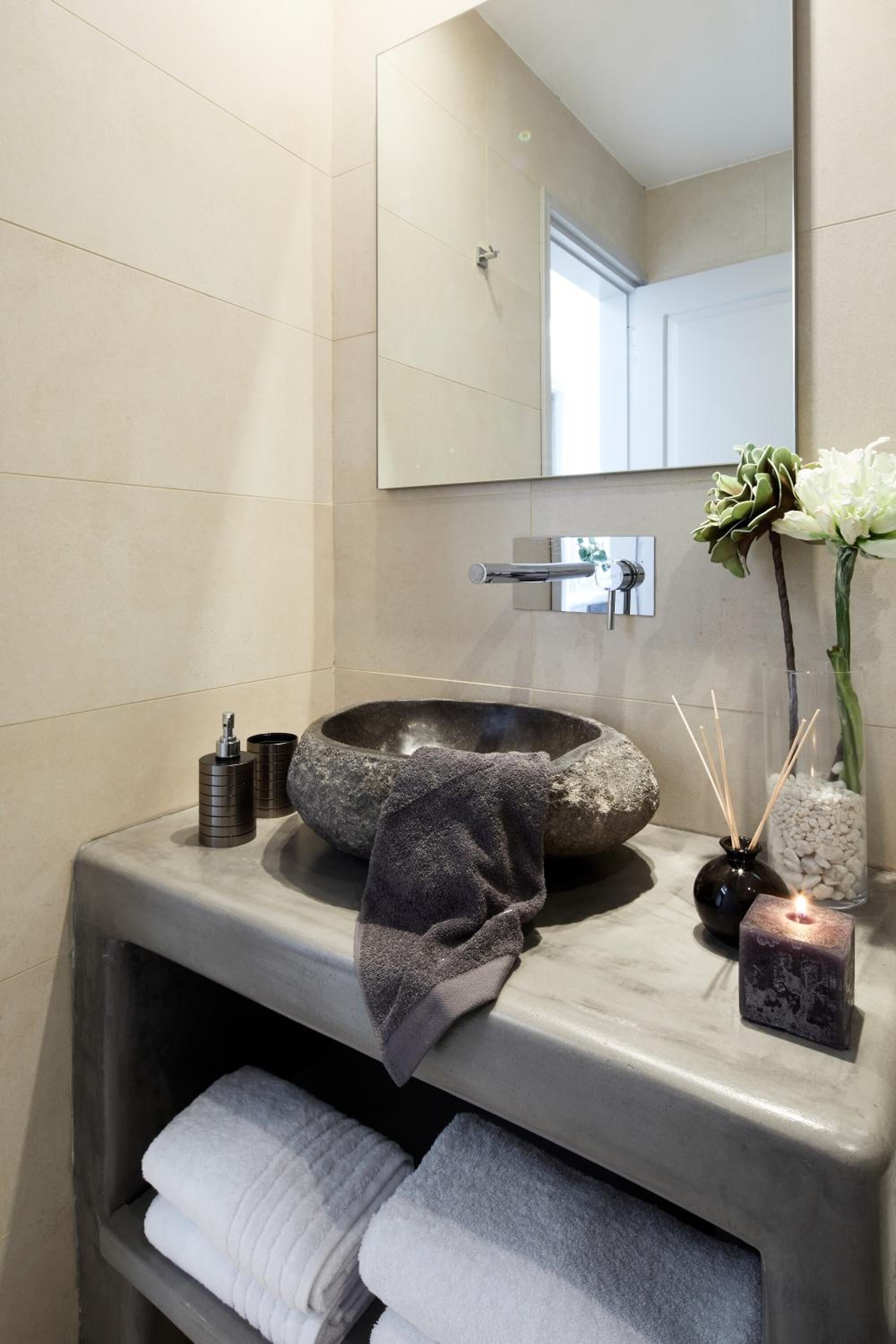 A modern bathroom with a stone sink, a towel rack, and a mirror.