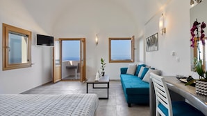 A modern room with a bed, a sofa, a dining table, and a view of the sea. - Alyvia Suites (Santorini)