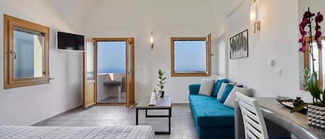 A modern room with a bed, a sofa, a dining table, and a view of the sea.
