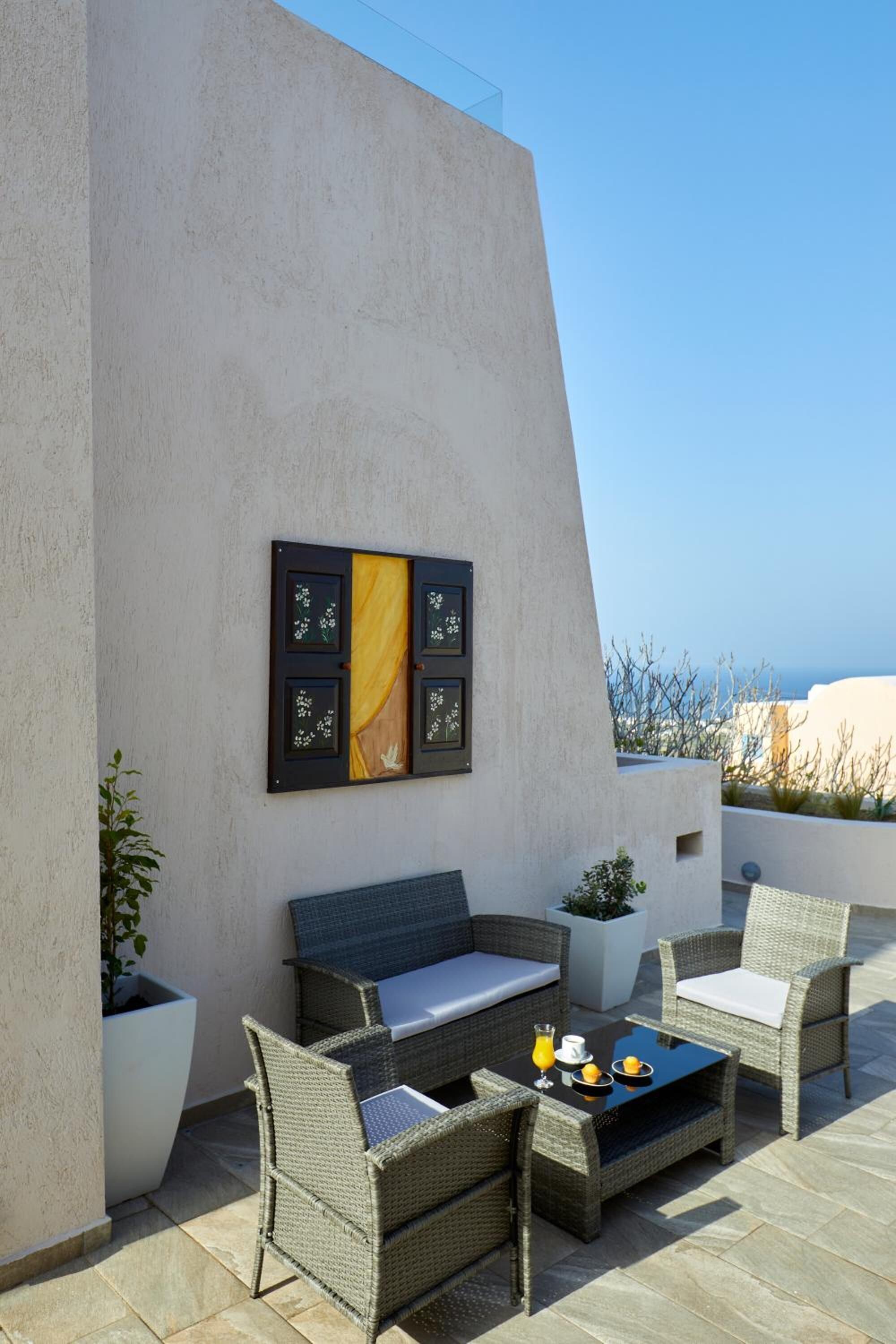 A modern outdoor seating area with wicker furniture and a glass table, set against a plain wall with a decorative panel.