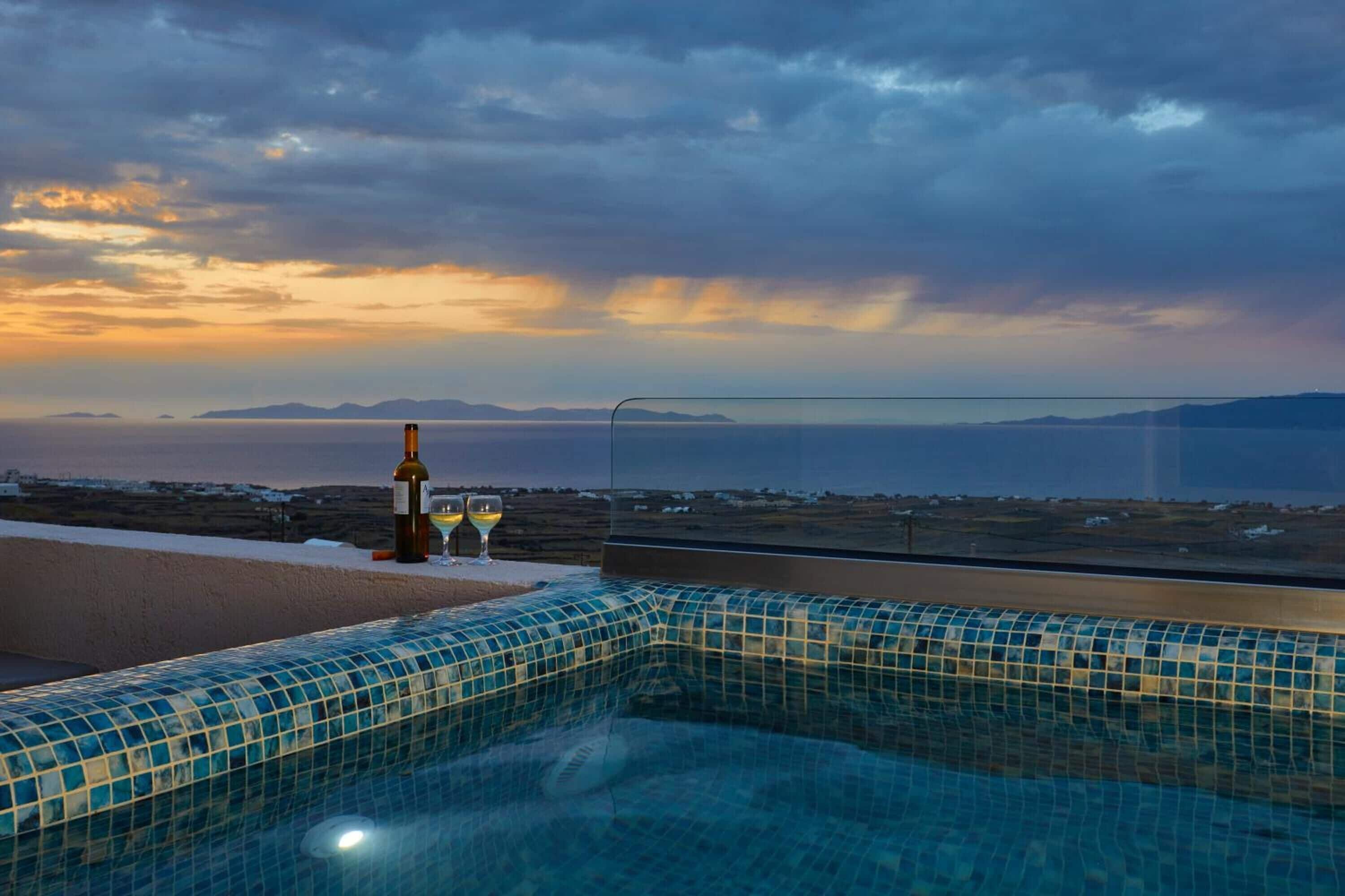 A pool with a tiled edge and a bottle of wine and two glasses on a table.