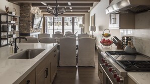 Une cuisine moderne dotée d’un îlot central, d’une cuisinière et d’un évier. On y trouve un mur en pierre et une grande fenêtre donnant sur la rue.