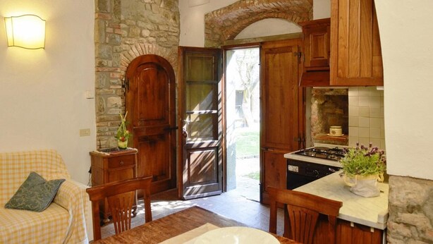 Une cuisine chaleureuse avec des murs en pierre, des meubles en bois et un coin repas agrémenté d’un canapé à carreaux.