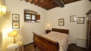 Une chambre avec un lit en bois, une table de chevet avec une lampe, une fenêtre et des tableaux encadrés au mur.