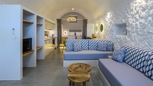 A modern living room with a sofa, two wooden coffee tables, and a kitchen area in the background. - Casa Tholari Al Mare (Αστυπάλαια)