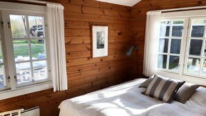 Une chambre dans un chalet en bois, avec un lit, deux fenêtres, un radiateur et une chaise.