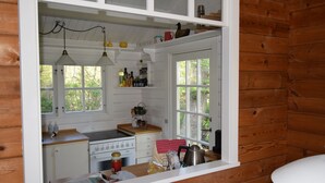 Une cuisine avec des meubles blancs, une cuisinière et un évier. On y trouve des luminaires suspendus et une fenêtre donnant sur des arbres.