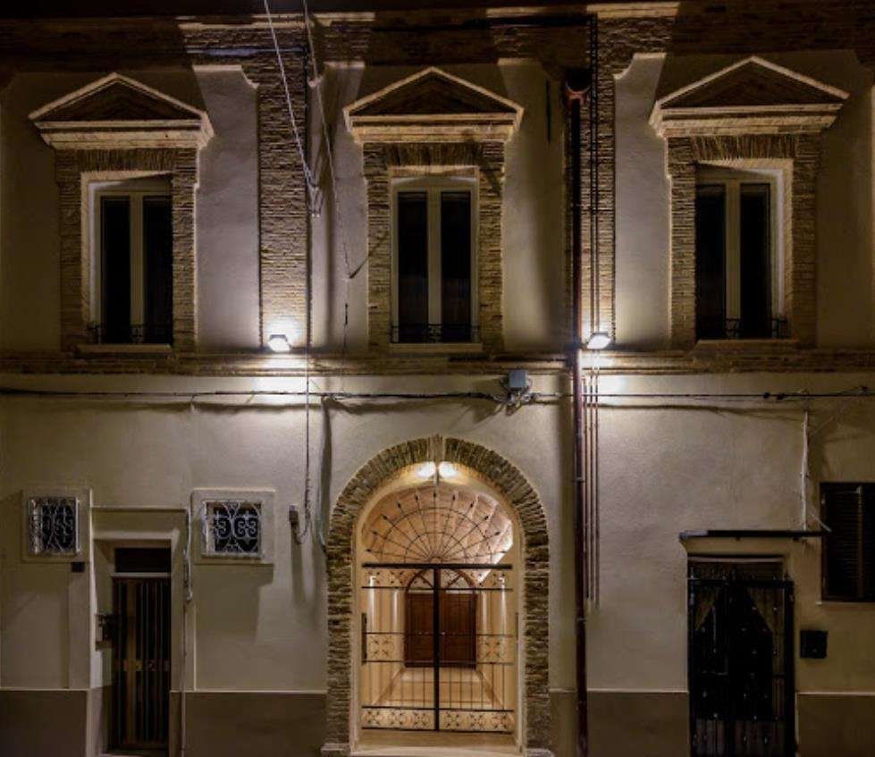 A building with a central arched entrance, multiple windows, and a door with a metal gate.