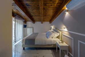 Une chambre avec un plafond en bois, un lit avec une literie blanche, une table de chevet et un luminaire fixé au mur.