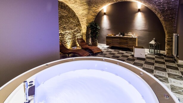 A spa area with a hot tub, lounge chairs, a wooden cabinet, and a stone wall. - Marie Claire Apartments Spa (Vasto)