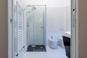 A modern bathroom with a glass-enclosed shower, a bidet, and a toilet.
