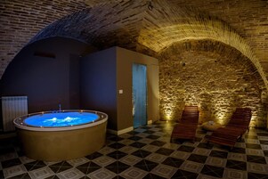 Un'area benessere con vasca idromassaggio, panche in legno e una parete in pietra.