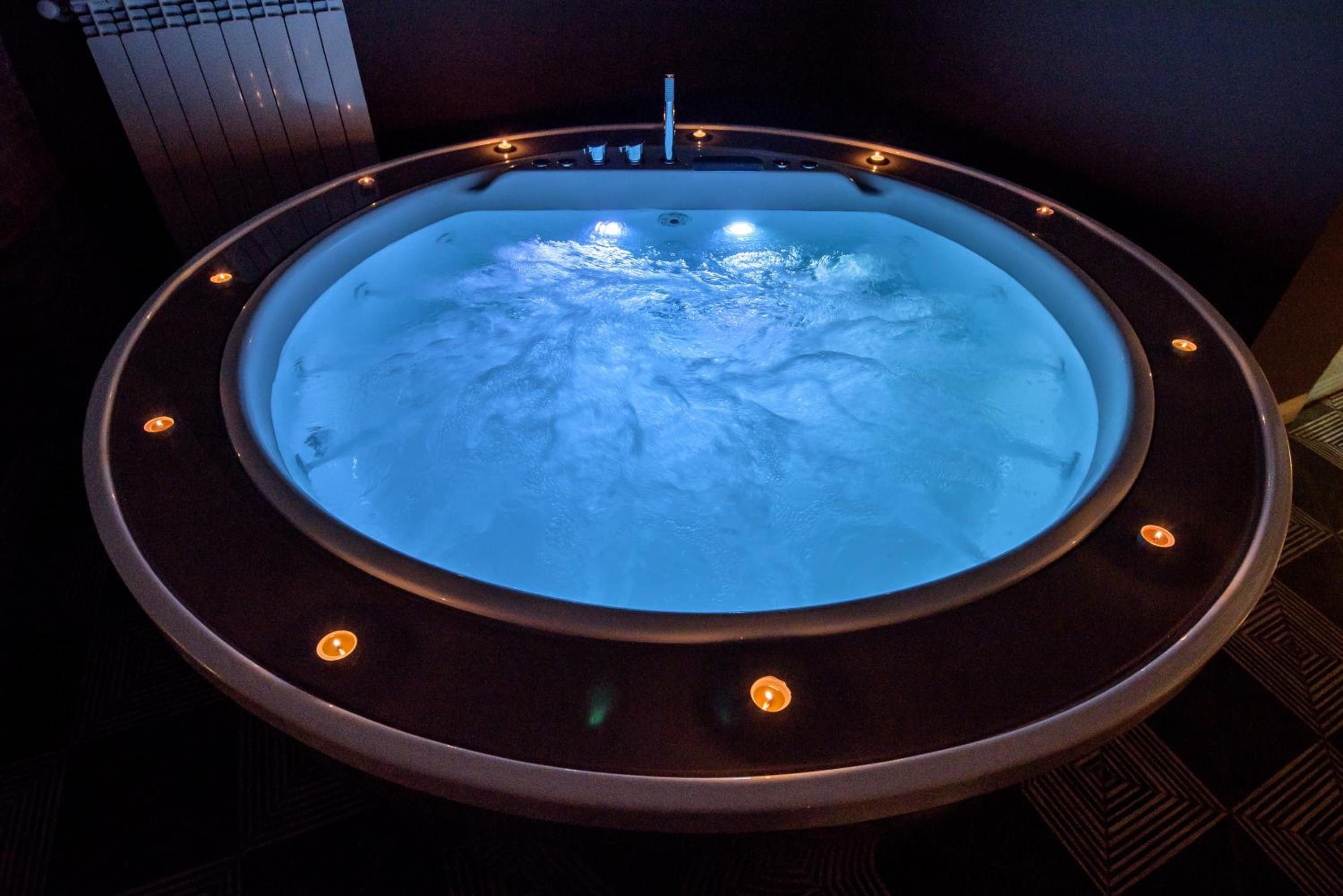 A circular hot tub with a blue light, surrounded by a dark wooden frame with small lights.