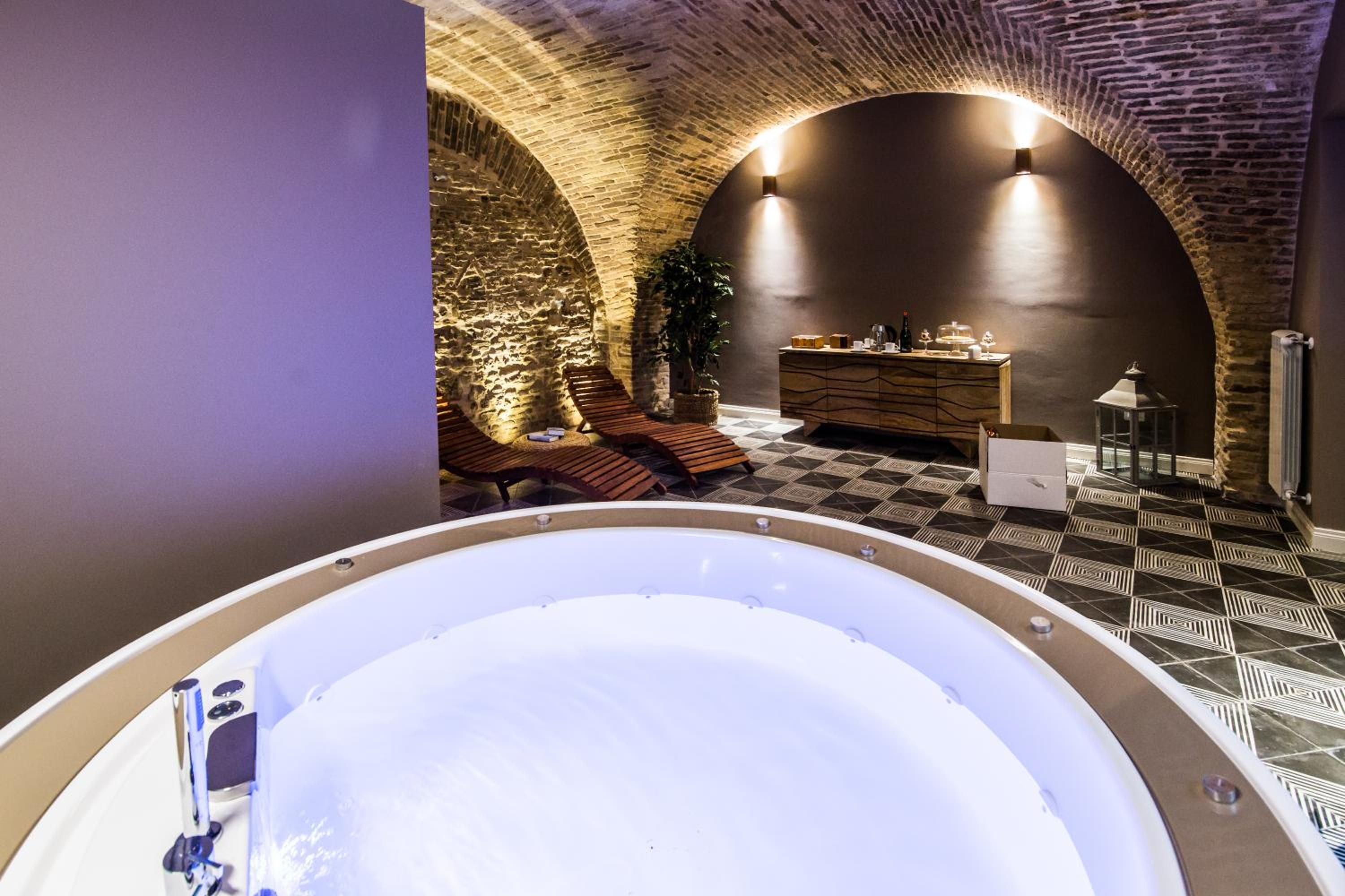 A spa area with a hot tub, lounge chairs, a wooden cabinet, and a stone wall.