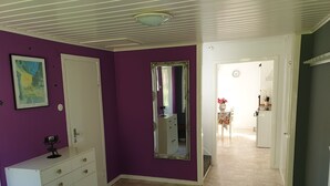 A room with purple walls, a white dresser with brass handles, a large mirror, and a door leading to another room.