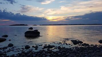 A rocky shoreline with calm water and a sunset in the background.