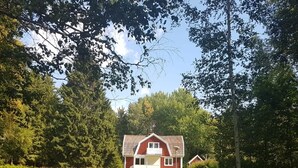 A red house with a white door and windows, surrounded by trees and grass.