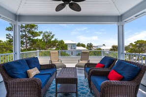 A covered outdoor seating area with wicker furniture and blue cushions, overlooking a residential neighborhood. - Family friendly beach home in Seacrest Beach/2 Living Areas/Resort style Lagoon Pool/Sleeps 14/WiFi! (Rosemary Beach)
