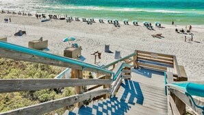 Una playa con una escalera de madera que baja a la arena, sillas y sombrillas.