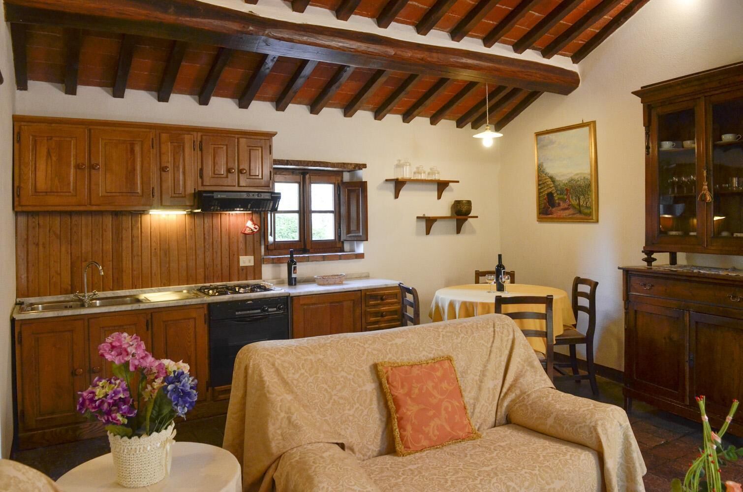 A cozy living room with a sofa, a dining table, and a kitchen area with wooden cabinets and a window.