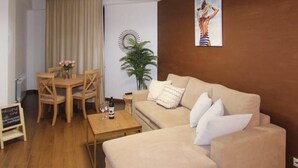 A modern living room with a beige sofa, wooden coffee table, and a dining table with chairs. There is a potted plant and a painting on the wall. - Apartment near in Republic square  (Yerevan)