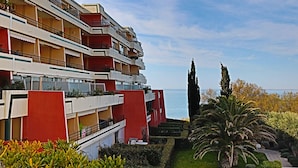 Un hôtel à plusieurs étages, doté de balcons, d’un jardin bien entretenu et offrant une vue sur la mer.