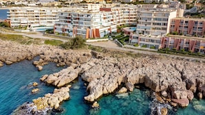 Une zone résidentielle côtière avec des immeubles à plusieurs étages, un littoral rocheux et des eaux d’un bleu limpide.