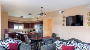 A modern living room with a sofa set, a dining table, and a kitchen in the background.
