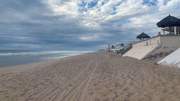 A beach with a staircase leading to a building with a thatched roof.