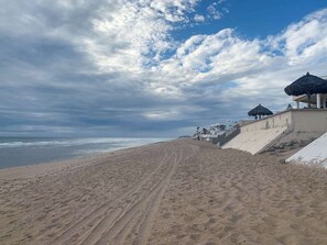 Une plage avec un escalier menant à un bâtiment dont le toit est recouvert de chaume.