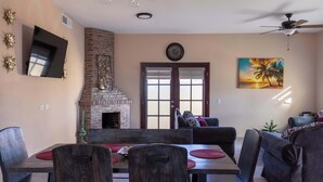 A dining area with a brick fireplace, a flat-screen TV, and a painting of a sunset.
