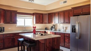 A kitchen with wooden cabinets, a stainless steel refrigerator, a large island with stools, and a window providing natural light.