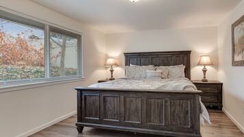 A bedroom with a wooden bed, two bedside tables with lamps, a window with blinds, and a painting on the wall.