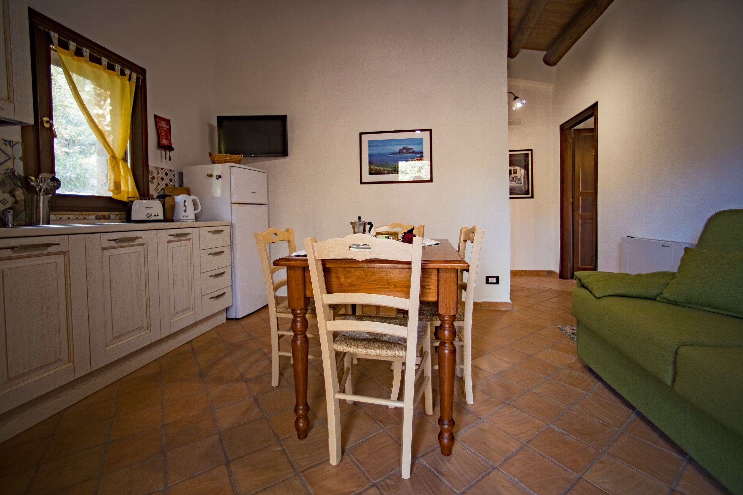Une cuisine de taille réduite comprenant une table à manger, des chaises, un canapé vert et un téléviseur.