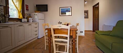 Une cuisine de taille réduite comprenant une table à manger, des chaises, un canapé vert et un téléviseur.