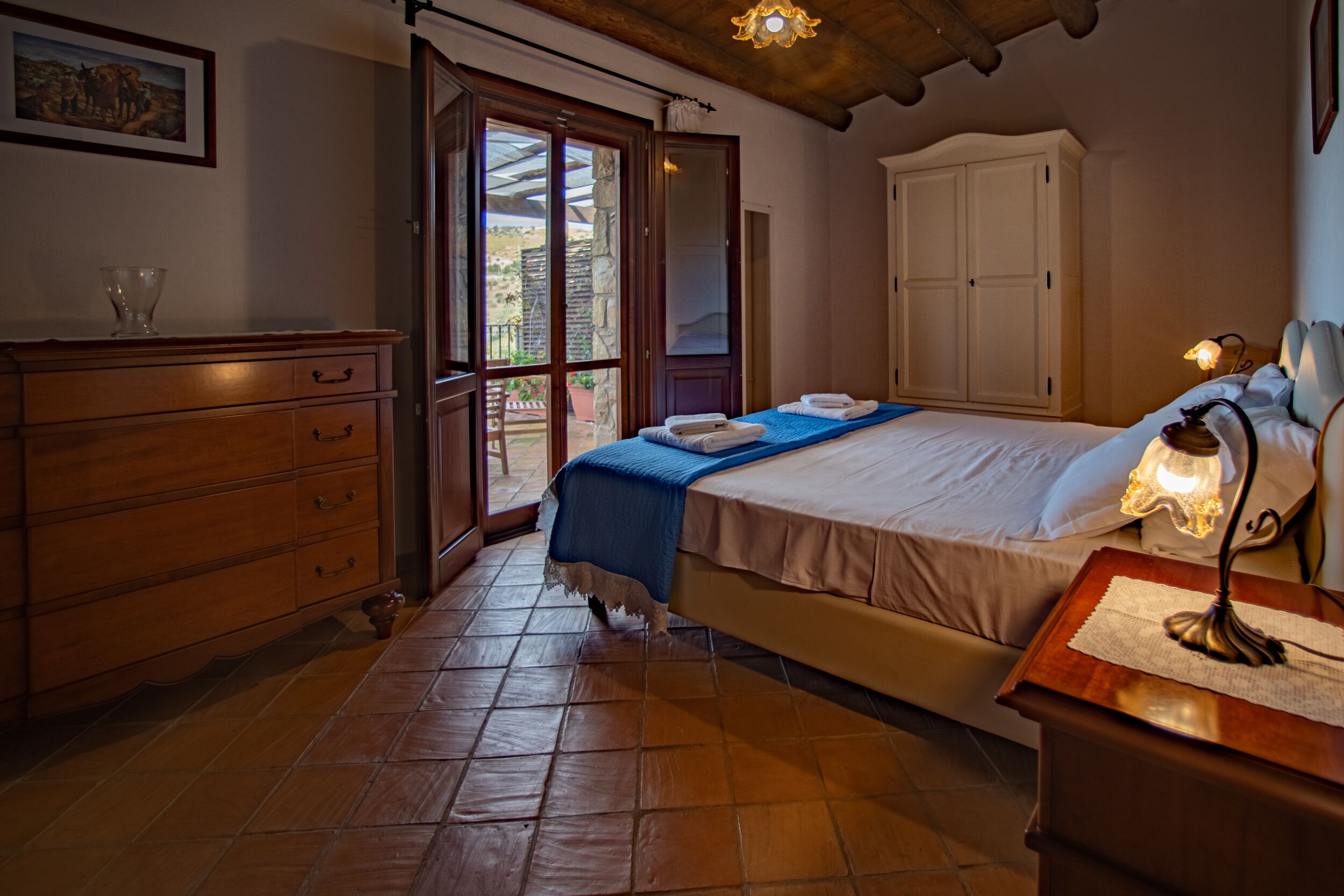 A bedroom with a bed, wooden dresser, and a nightstand with a lamp.