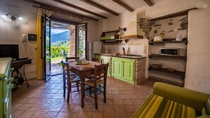 A rustic kitchen with green cabinets, a dining table with chairs, and a view of greenery outside. - Poggio Pozzetti (Lascari)