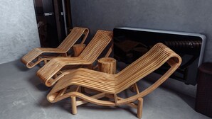 Three wooden lounge chairs with a unique design, positioned near a radiator in a room with a concrete floor and a textured wall. - ABK Hotel (Atyrau)