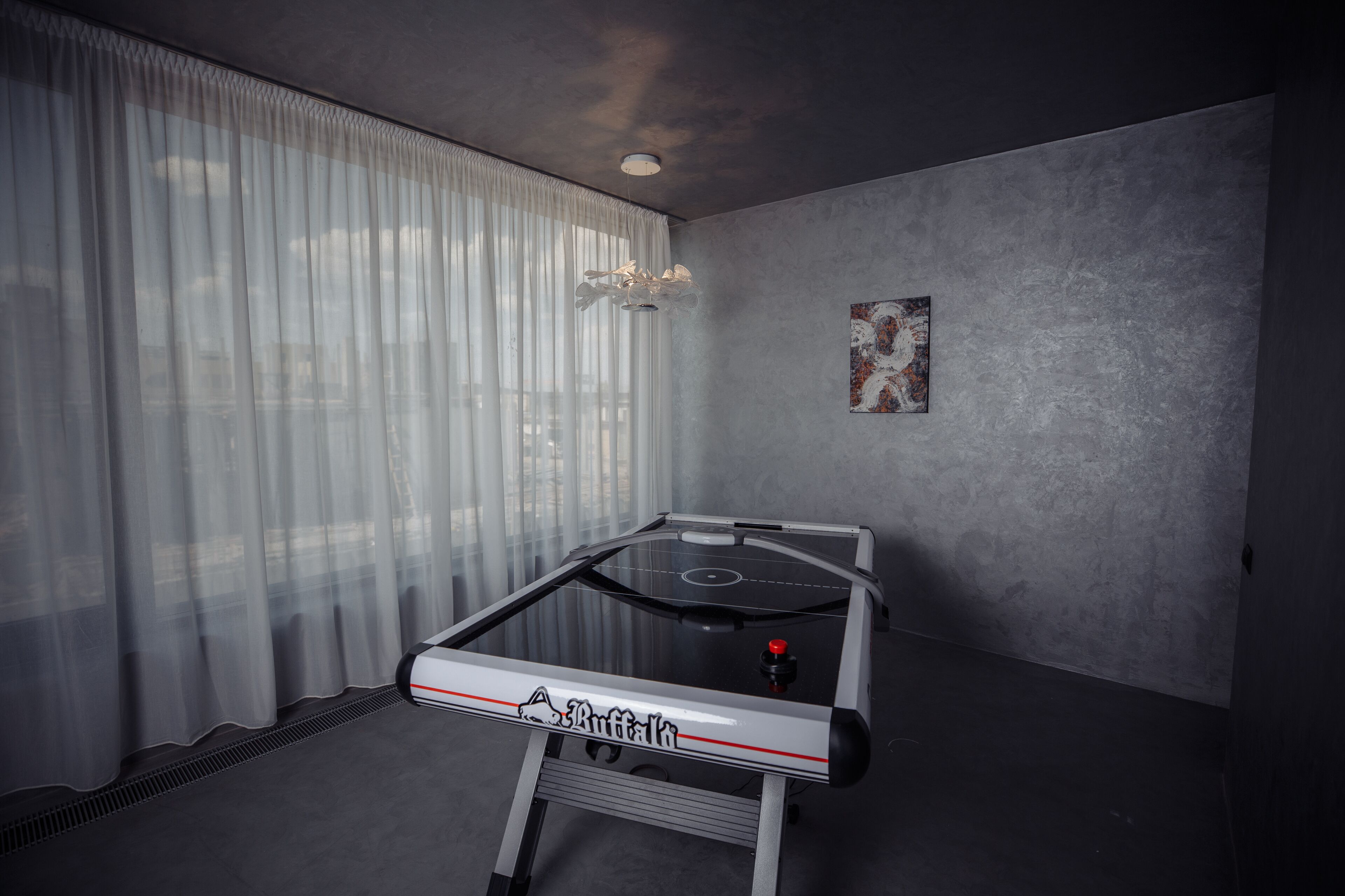 A room with a foosball table, a ceiling light, and a painting on the wall.