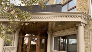 A building entrance with a covered porch, stone walls, and a set of stairs leading up to the doors. - ABK Hotel (Atyrau)