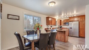 Una cocina moderna con armarios de madera, un refrigerador de acero inoxidable y un comedor con mesa de mármol y sillas de cuero.