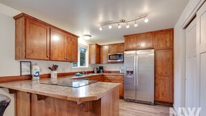 Una cocina moderna con armarios de madera, un refrigerador de acero inoxidable, un microondas y una encimera de granito.