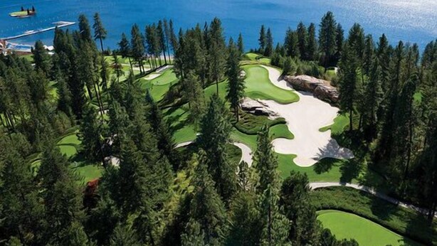 Un campo de golf con un lago al fondo, rodeado de un bosque denso.