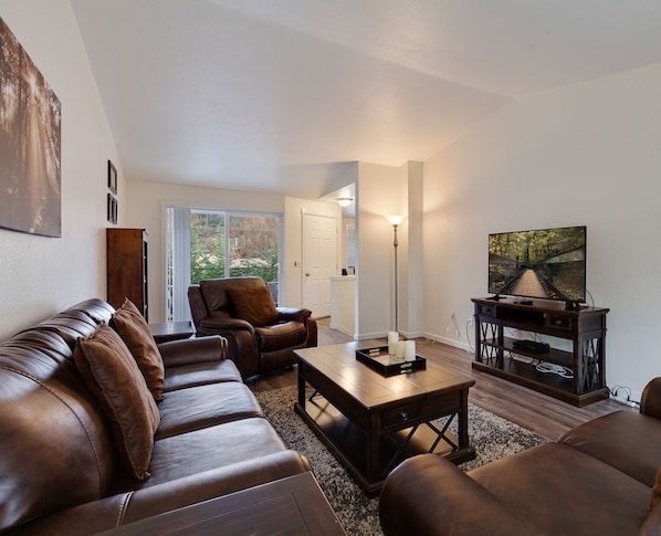 A modern living room with leather sofas, a coffee table, and a TV on a wooden stand. - Duplex Home—5 Min Walk to Sanders Beach & Trails, Spacious Family Room, Just 1 Mile to Downtown! (Coeur d'Alene)