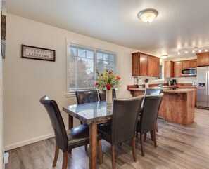 A modern kitchen with wooden cabinets, a stainless steel refrigerator, and a dining area with a marble table and leather chairs. - Duplex Home—5 Min Walk to Sanders Beach & Trails, Spacious Family Room, Just 1 Mile to Downtown! (Coeur d'Alene)