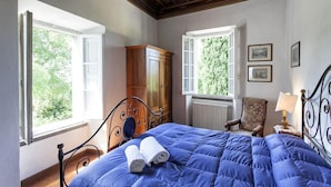A bedroom with a bed, a wooden wardrobe, a chair, and a window with a view of greenery. - VILLA SERENA x6 Beautiful villa surrounded by nature, with swimming pool just 1 km from Cortona (Cortona)