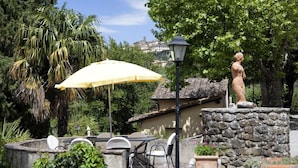 An outdoor patio with a table and chairs, a yellow umbrella, and a statue. - VILLA SERENA x6 Beautiful villa surrounded by nature, with swimming pool just 1 km from Cortona (Cortona)