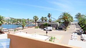 Vista costera con un puerto deportivo, palmeras y un edificio blanco de techo plano.