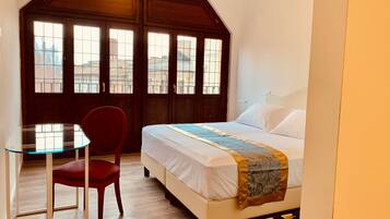 Ein Schlafzimmer mit einem Bett, einem roten Sessel, einem Glastisch und einem großen Fenster mit Blick auf Gebäude.