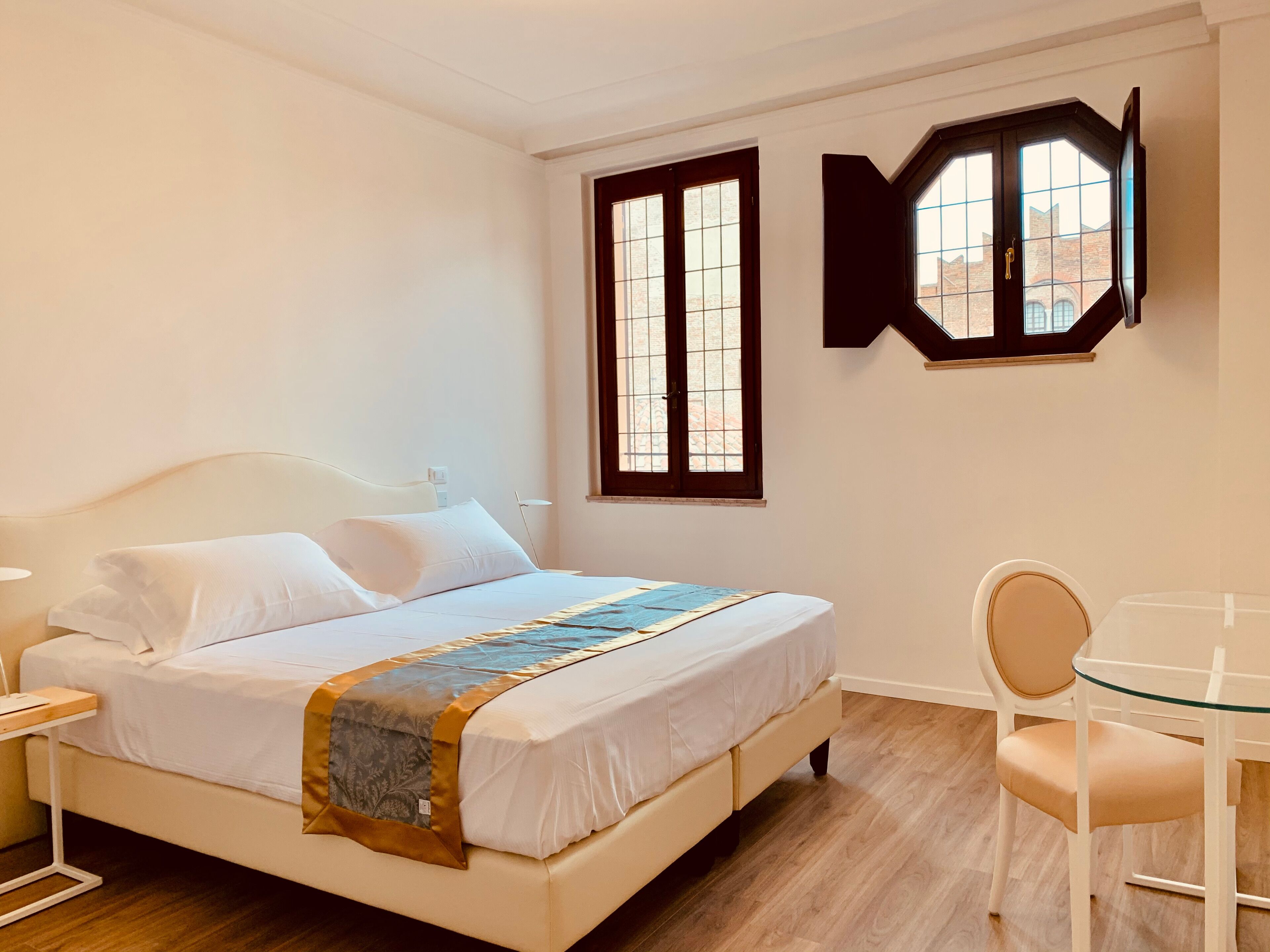 A bedroom with a bed, bedside table, chair, and a window with a view of buildings.